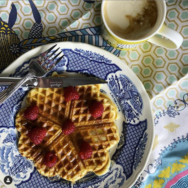 Waffle with berries on plate with coffee to the side.