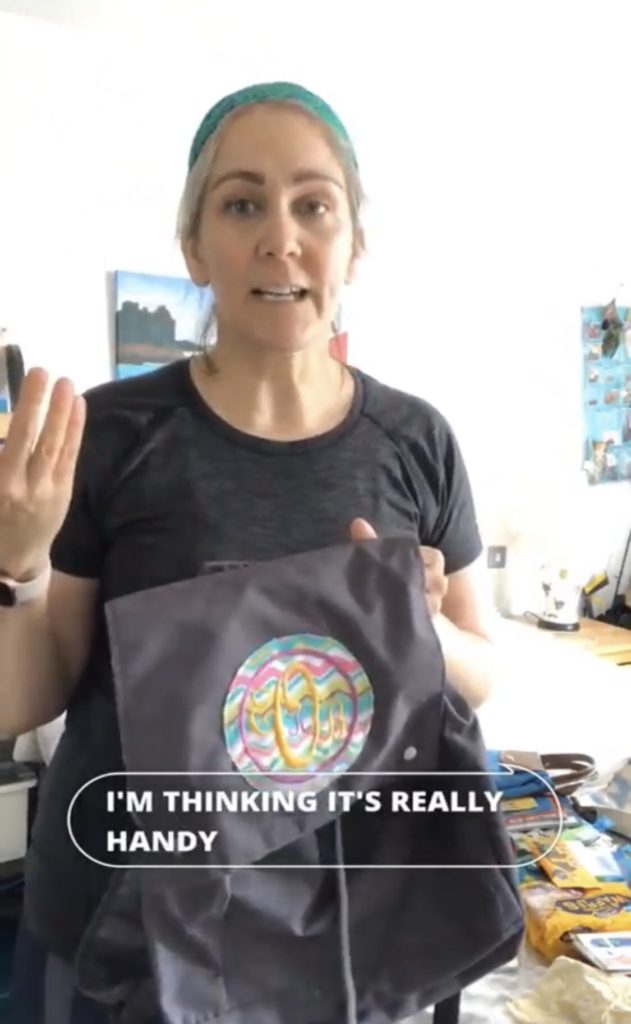 Screenshot photo from video of a woman standing with a backpack in one hand and gesturing with the other hand. Caption reads: "I'm thinking it's really handy."
