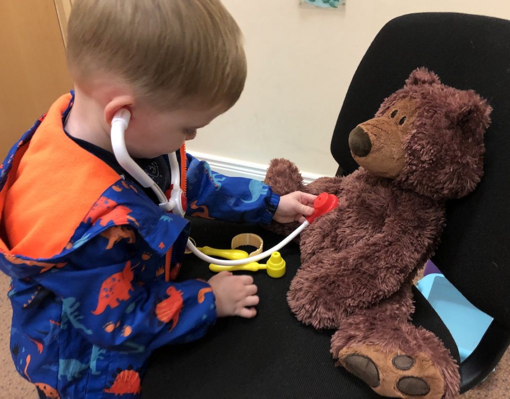 A child using a toy stethoscope to listen to a stuffed animal bear's heartbeat.