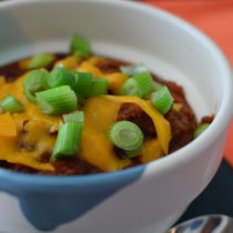 Bowl with beef chili topped with cheddar cheese and chopped scallions