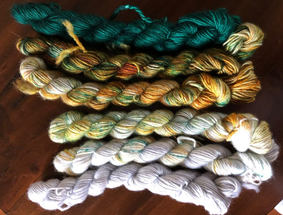 Yarns mini skeins with deep green on the left then rusty colors then off-white.