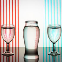 Red and blue stripes on white background. Lines refracted through glassware filled with water. Middle glass reverses color of stripes for interesting effect. Yes, center glass piece is upside down.