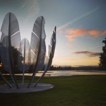 Tall metal feathers in a bowl-shape against a colourful sunset sky in Ireland