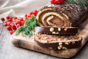 Chocolate yule log cake with red currant on wooden background