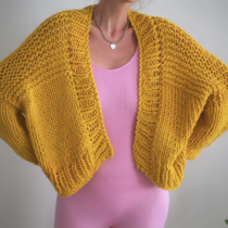 Figure in pink unitard wearing cheerful hand knit mustard yellow chunky cardigan with hands on hips