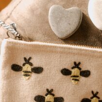 An embroidered zippered pouch adorned with little bees. Two heart-shaped stones appear to have emerged from the bag in time for the photo. Image by Melissa di Rocco