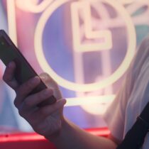Hand holding a phone with neon lights in the background blurry