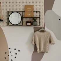 Peg board and mural wall with a home decor style in muted earthy colors. A presumably hand knit short sleeve sweater hangs slightly off centre. Photo by Toa Heftiba