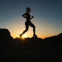 Silhouette of a person trail running with the sunrise or sunset behind.