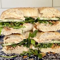 Sesame seed bagel with smoked salmon spread, rocket, cucumber, and fried onions for a savory and sweet sandwich.